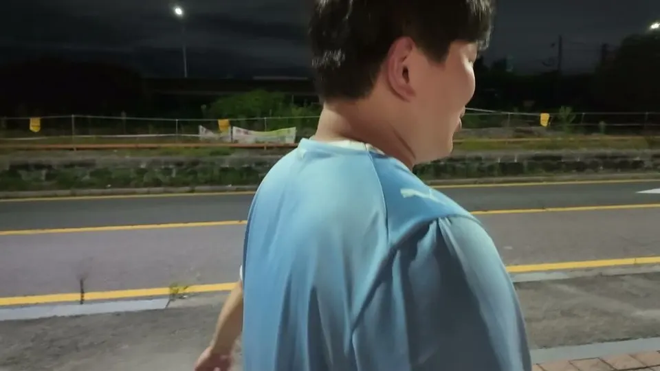 A friend in a light blue football shirt walking ahead along a dark roadside