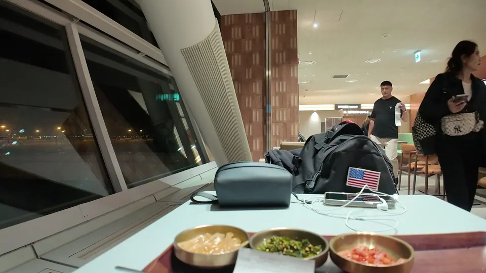 Three small brass bowls of side dishes on a table by a dark airport window at Incheon