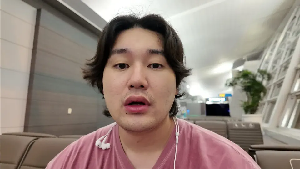 Eddie talking to the camera in an empty gate with earphones hanging off his collar