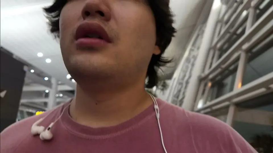 Eddie talking to the camera with earphones draped over his shoulders in an empty Incheon gate area