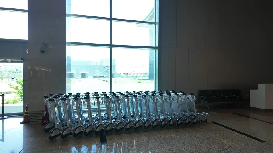 A long line of silver luggage trolleys parked along a glass wall in the Cam Ranh arrivals hall