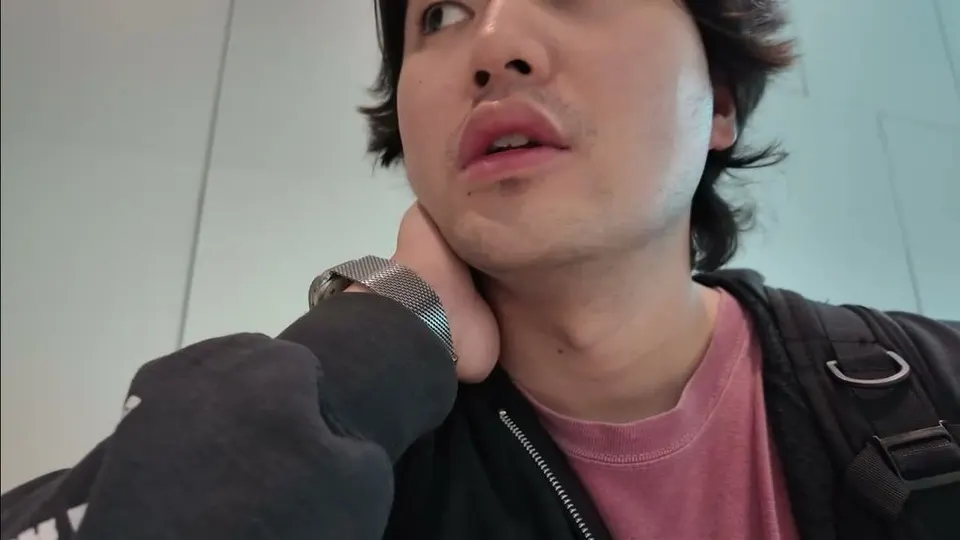Eddie looking up in the bright white arrivals hall at Cam Ranh, backpack strap on his shoulder