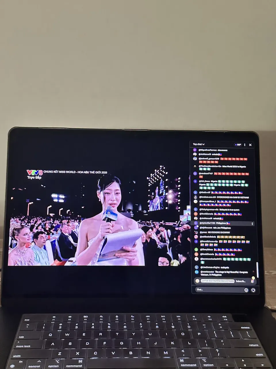 A laptop on a table streaming the Miss World final on VTV8 with a live chat column of flags