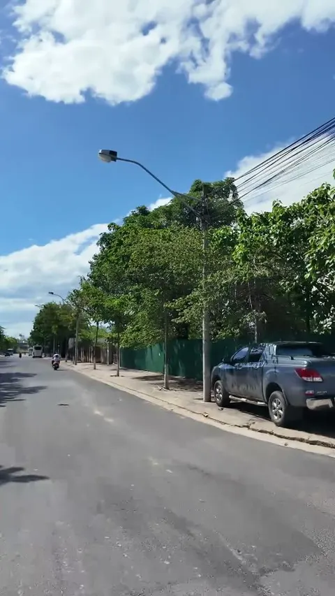 Wide empty two lane road under a big blue sky, a single distant rider on the left and a pickup truck parked by a green fence