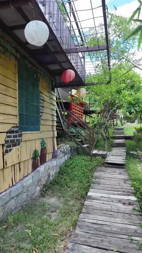 Yellow wooden house with peeling paint and paper lanterns hanging under the eaves, boardwalk running past it uphill