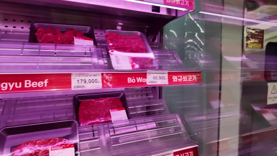Supermarket fridge with trays of wagyu beef under a red shelf strip in Korean