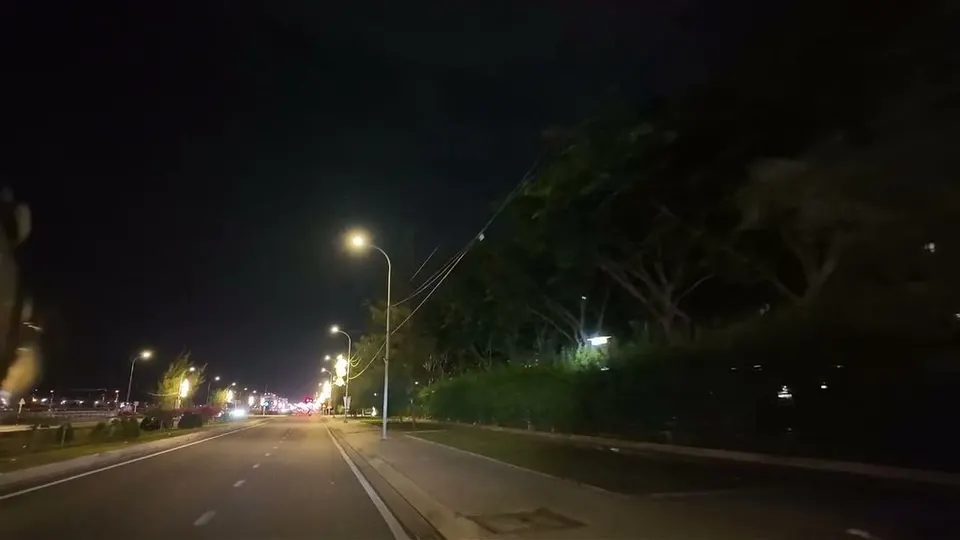 Wide empty boulevard at night with streetlights curving into the distance and trees along the right side