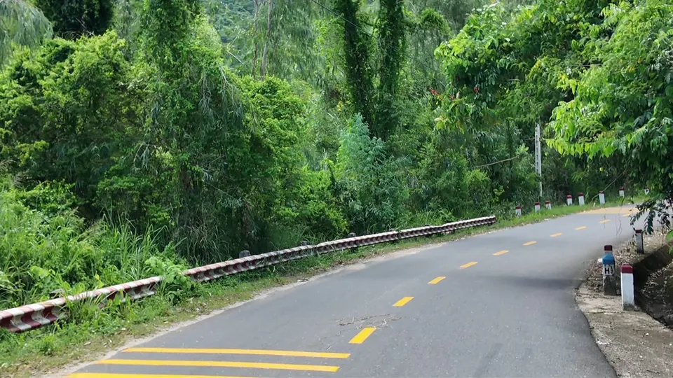 A shaded bend in a narrow road with a red and white barrier on the left
